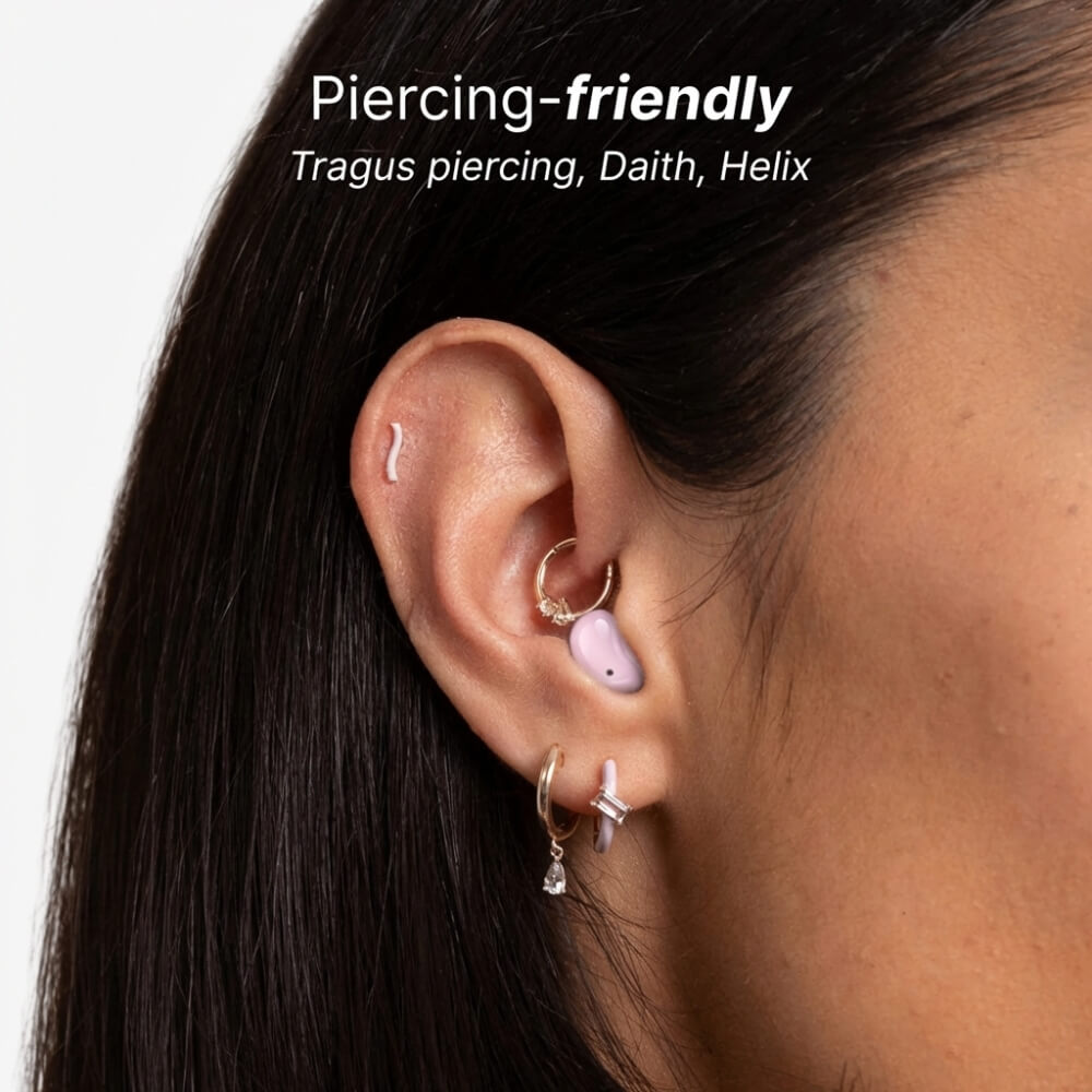 Close-up of a woman's ear featuring a white wavy helix piercing a gold hoop daith piercing and a pastel purple earbud in the tragus